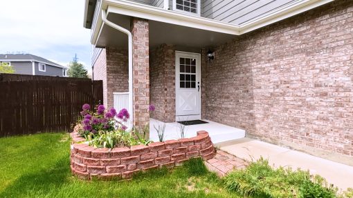 Brick home entrance with a downspout running down beside a raised planting bed