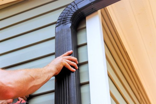 Hand checking a dark downspout fitted against house siding