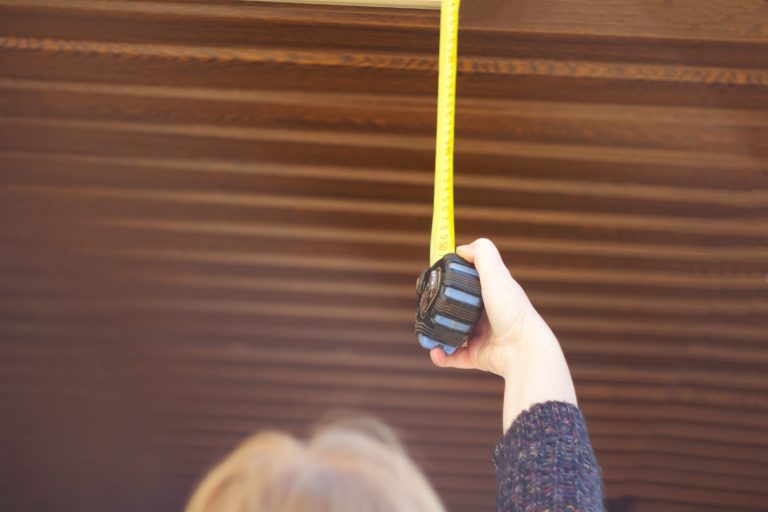 Hand holding a tape measure extended up a wall