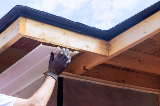 Gloved contractor fitting a white soffit panel along a roof edge