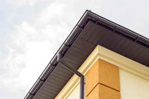 Brown gutter and downspout along the fascia of a house corner
