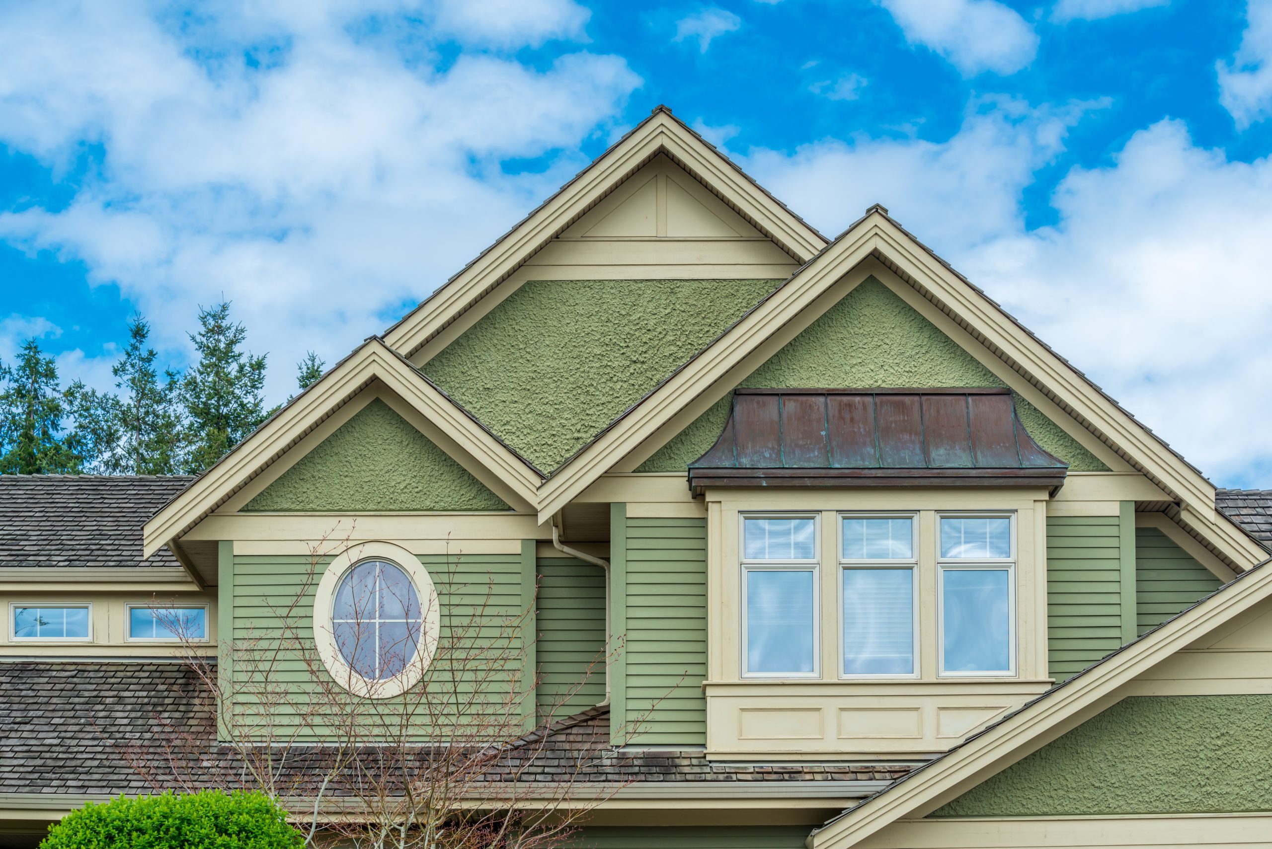 Home exterior showing a standing-seam metal bay roof beside shingle roofing with gutters