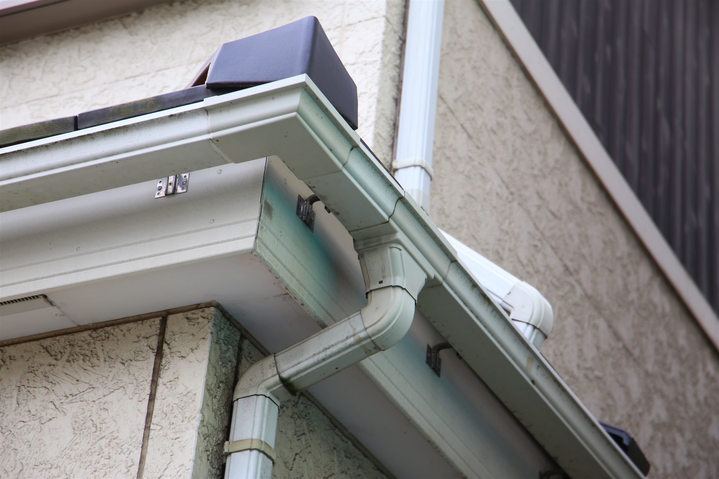 White gutter corner and downspout under the eave of a house